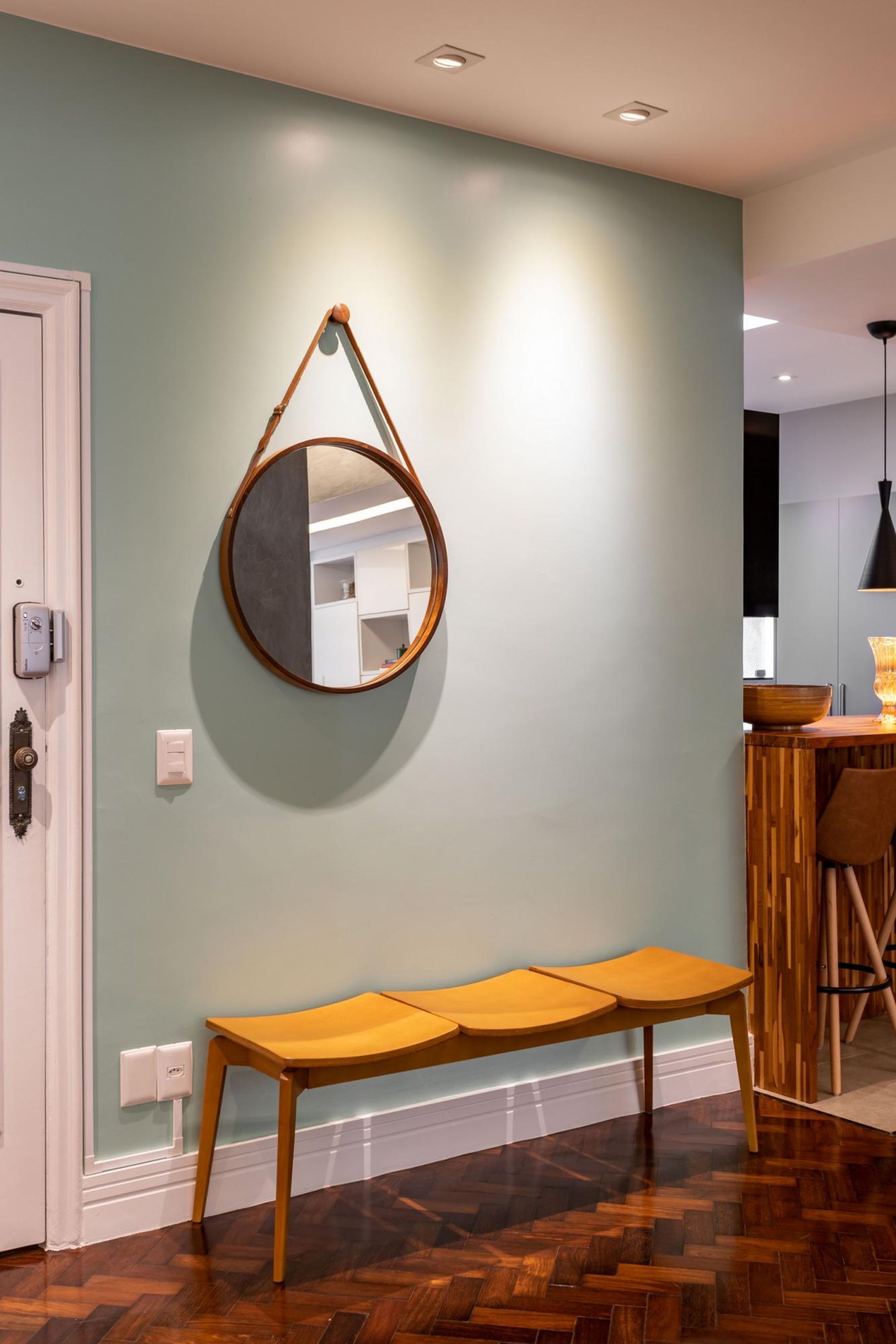 Una habitación con un banco de madera, un espejo colgante y una mesa de madera.