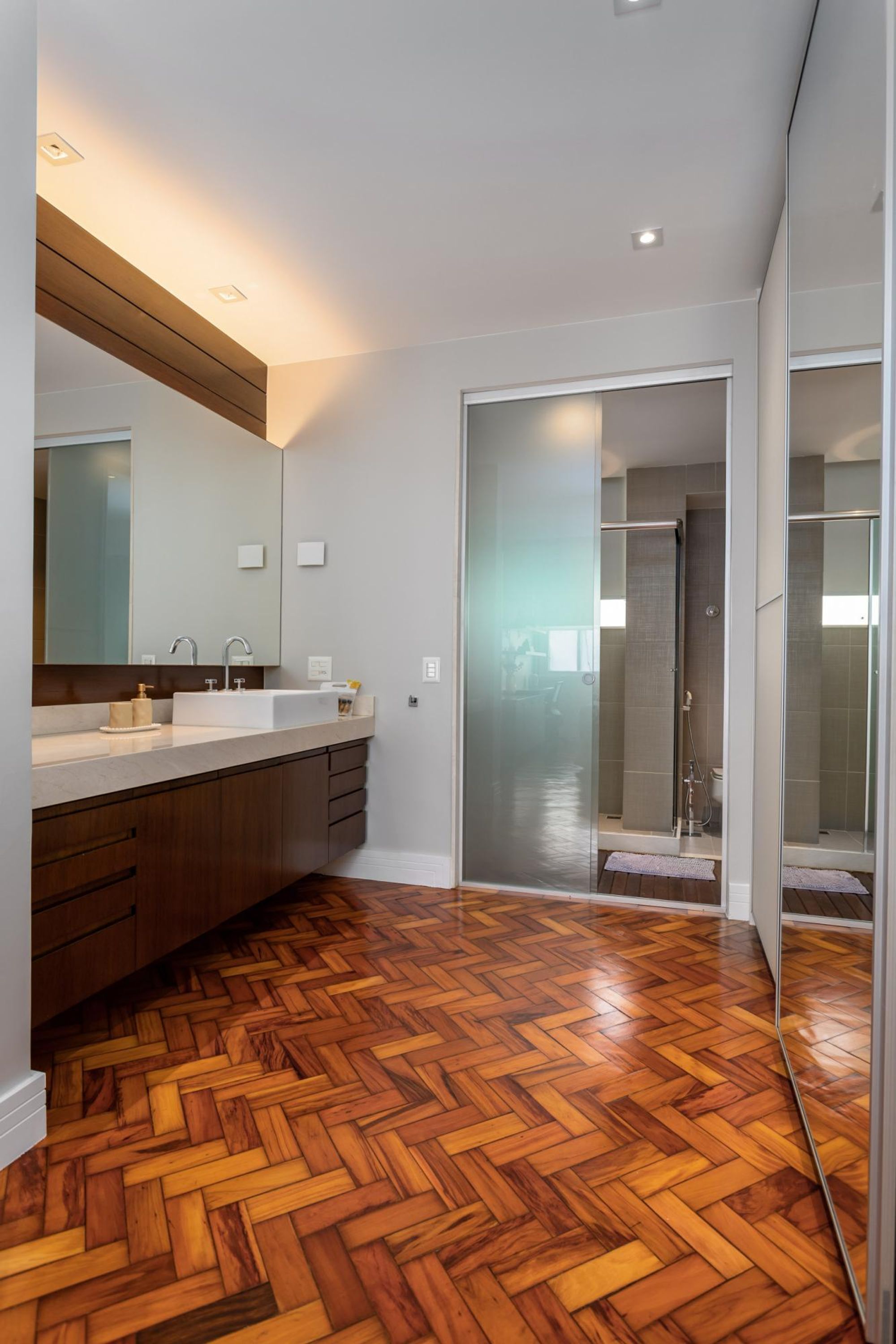 A modern bathroom with a wooden herringbone floor, a large mirror, and a walk-in shower.