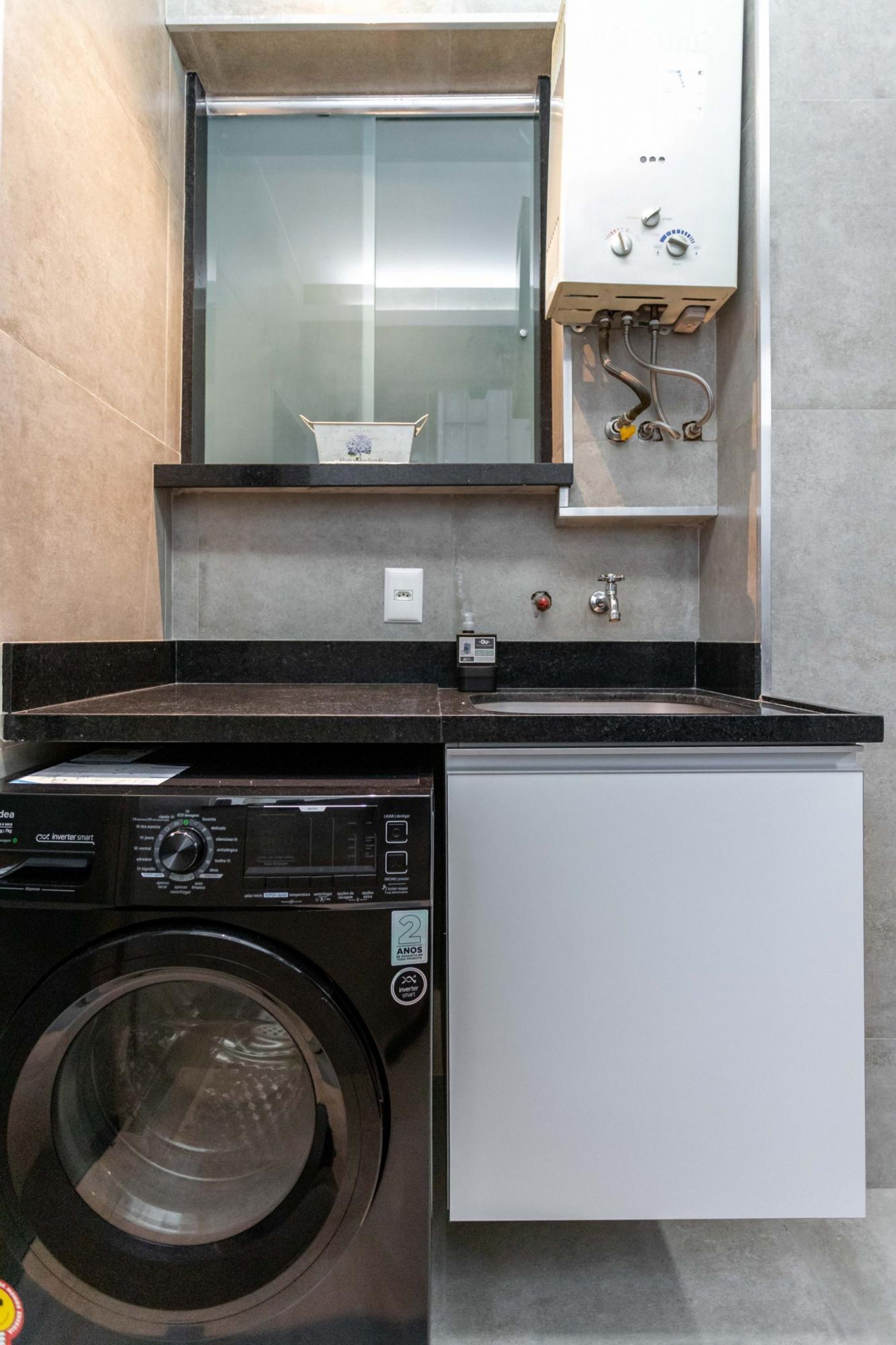 A compact laundry room with a front-loading washing machine, a small cabinet, and a built-in heater.