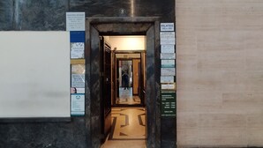 Un pasillo con suelo de baldosas que conduce a una habitación con una puerta. Hay letreros en las paredes y una lámpara sobre la puerta.