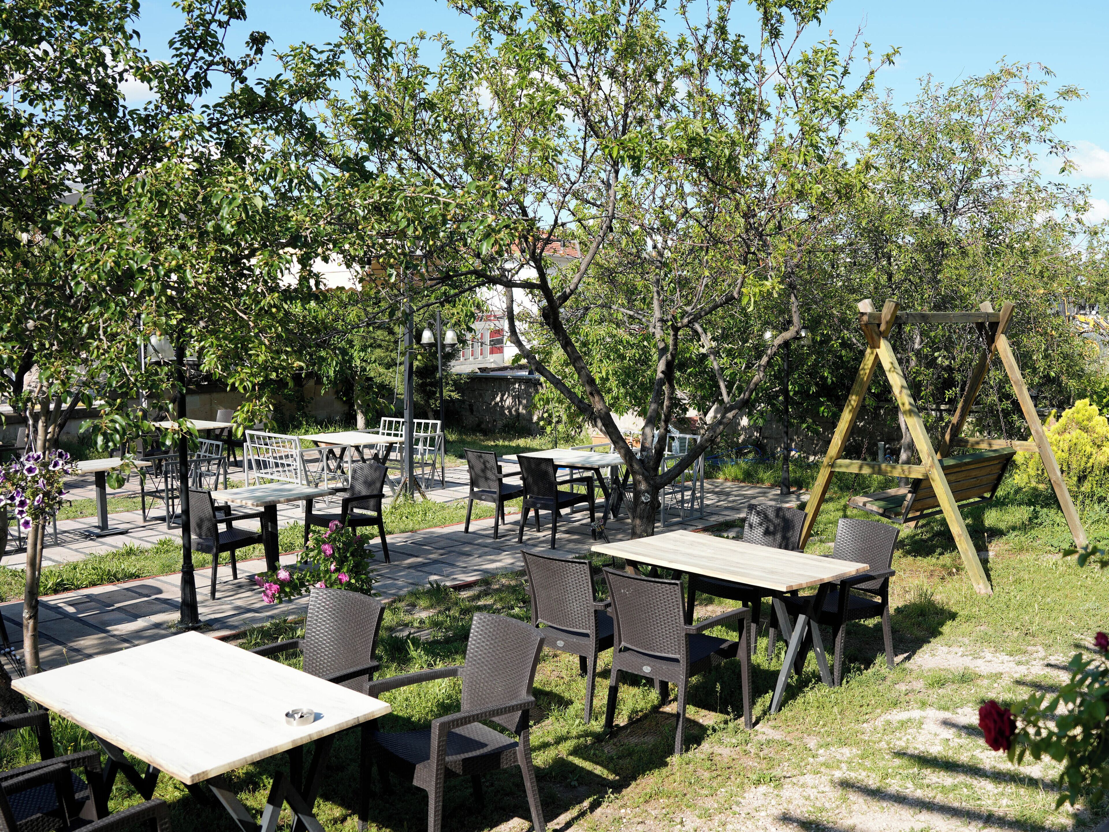 An outdoor seating area with tables and chairs, surrounded by trees and greenery.