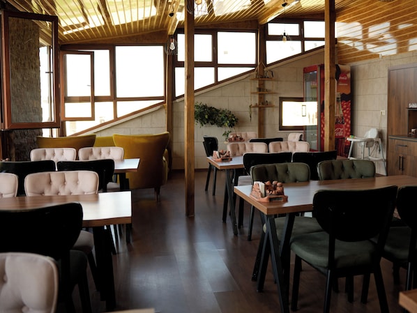 A restaurant with high ceilings, large windows, and a variety of seating options including booths and tables. - Cappadocia Panda Garden House (Nevsehir)