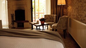 A hotel room with a fireplace, a bed, a table with a plant, two armchairs, and a lamp. - Cappadocia Panda Garden House (Nevsehir)