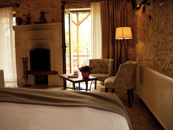 A hotel room with a fireplace, a bed, a table with a plant, two armchairs, and a lamp.
