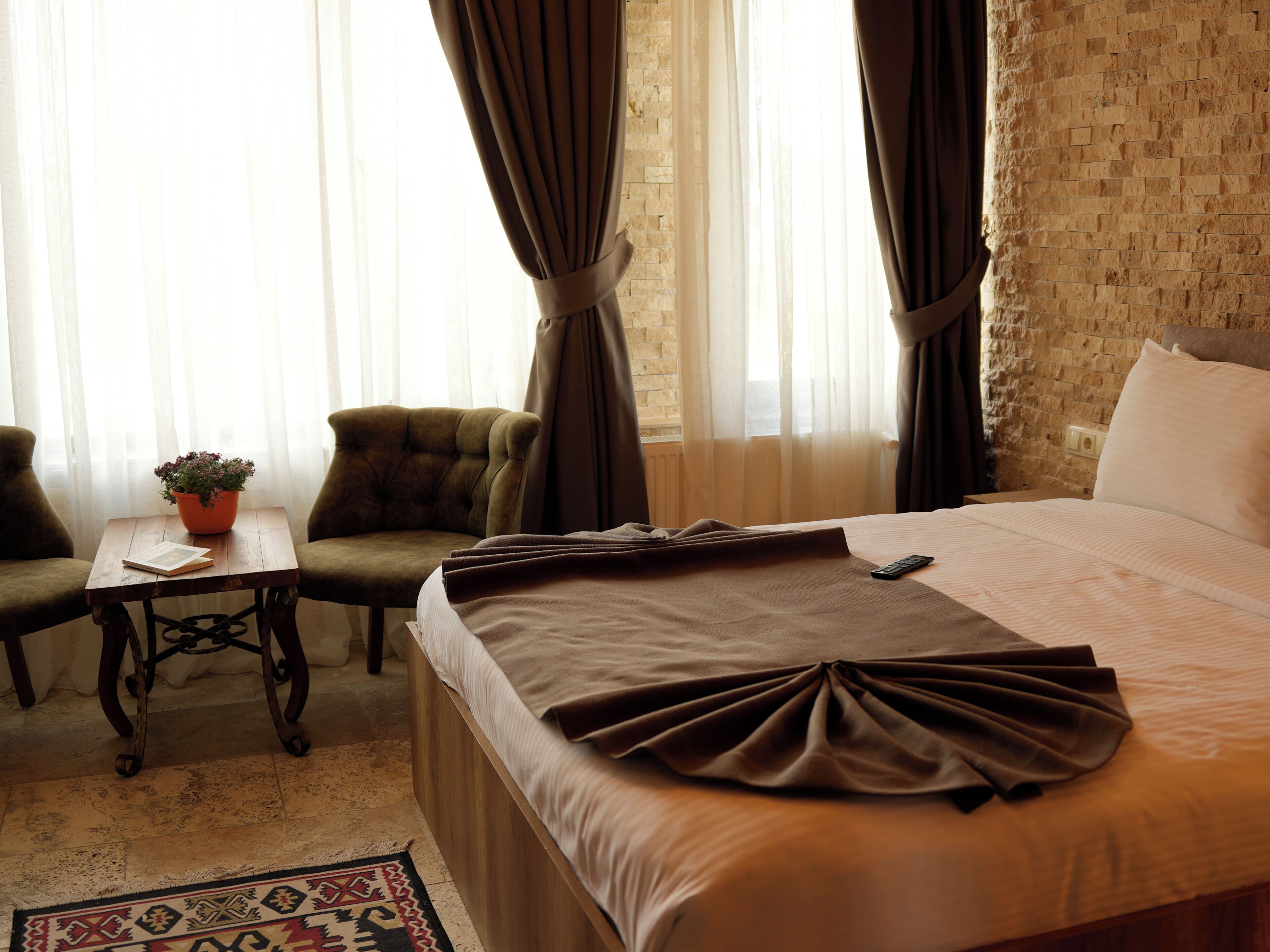 Habitación de hotel con cama, una silla, una mesita con una planta y una ventana con cortinas.