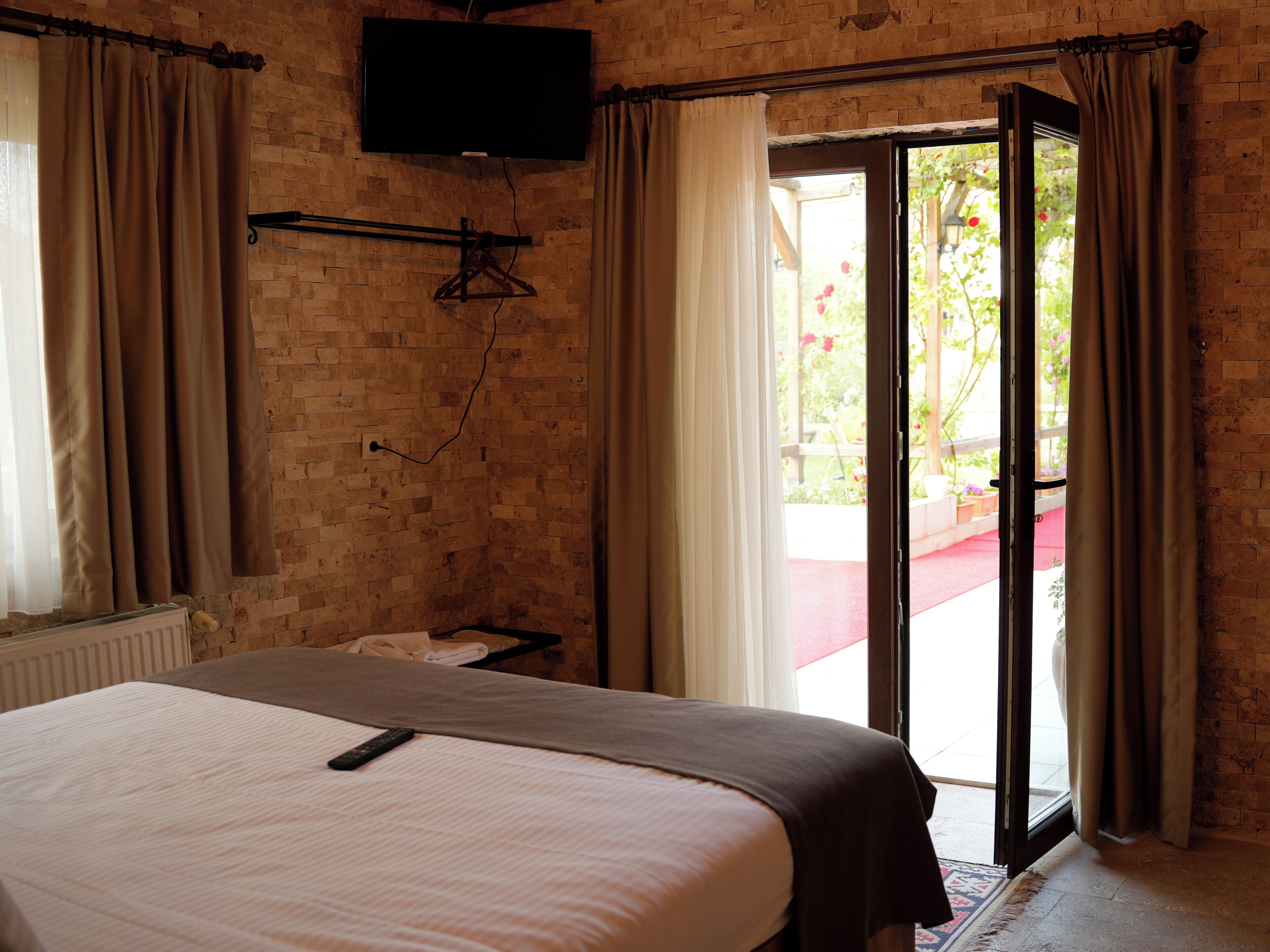 Habitación de hotel con cama, televisor montado en la pared y puerta corrediza de vidrio que da a un área exterior.