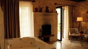 A room with a large bathtub, a fireplace, a chair, and a table with a lamp. - Cappadocia Panda Garden House (Nevsehir)