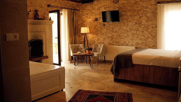 A hotel room with a brick wall, a fireplace, a bed, a chair, a table with a lamp, and a TV mounted on the wall. - Cappadocia Panda Garden House (Nevsehir)