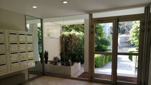 Een ruime lobby met een groot metalen archiefkast, een glazen wand met uitzicht op een tuin, en een glazen deur die naar buiten leidt.