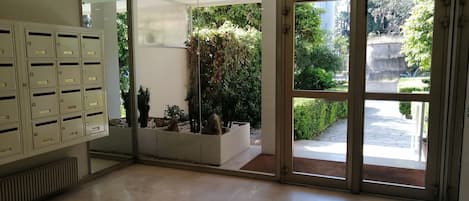 A spacious lobby with a large metal filing cabinet, a glass wall with a view of a garden, and a glass door leading outside.