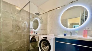 Een moderne badkamer met een douchecabine van glas, een ingebouwde wasmachine, een wastafelmeubel met spiegel en een wastafel.