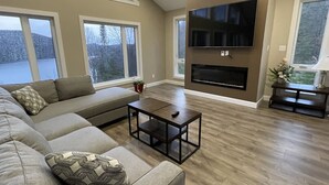 Ein modernes Wohnzimmer mit einem großen Sofa, einem Couchtisch, einem Kamin und einem an der Wand montierten Fernseher.
