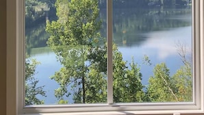 Ein Zimmer mit großem Fenster und Blick auf einen See, der von dichtem Wald und Hügeln umgeben ist.