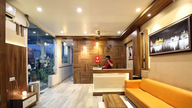 A hotel reception area with a wooden reception desk, a receptionist, a sofa, and a large framed picture on the wall. - OYO Rooms 099 Ram Talai Temple (Amritsar)