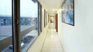 A corridor with large windows, a tiled floor, and a framed picture on the wall. - OYO Rooms 099 Ram Talai Temple (Amritsar)