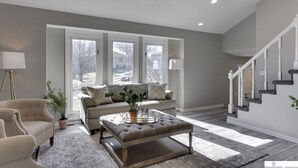 A living room with a sofa, ottoman, and armchair, a coffee table, and a staircase. - Newly Remodeled Home - 20 minutes from anywhere in Omaha! (Omaha)