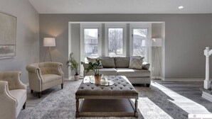 A spacious living room with a large window, a sofa, two armchairs, a coffee table, and a floor lamp. - Newly Remodeled Home - 20 minutes from anywhere in Omaha! (Omaha)