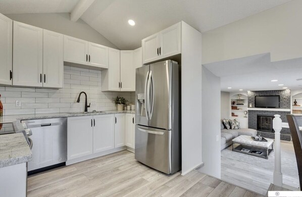 A modern kitchen with white cabinets, a stainless steel refrigerator, and a dining area with a sofa and coffee table.