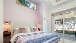 Une chambre dotée d’un grand lit, d’une table de chevet avec une lampe et d’une porte-fenêtre coulissante donnant sur un espace extérieur.