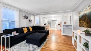 En moderne stue med en sort modulsofa, et lille sofabord og et spiseområde med et hvidt bord og stole.