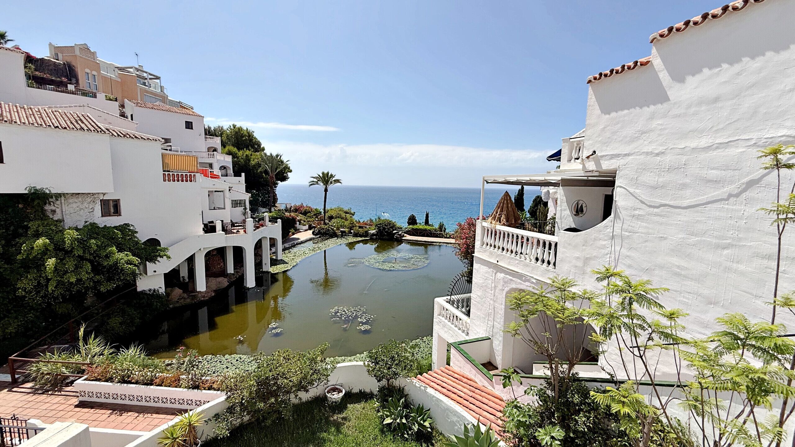 A coastal hotel with a pool, white buildings, and a view of the sea.