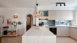 Una cocina moderna con una isla de mármol, iluminación colgante y vista al área de comedor.