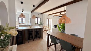 Una cocina moderna con una isla central, luces colgantes y un comedor con sillas.