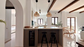 Una cocina moderna con una isla central, luces colgantes y un comedor con una silla.