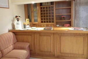 Ein Empfangstresen mit einem Holzkasten, einem gestreiften Sofa und einem kleinen Tisch mit einer Vase und Broschüren.