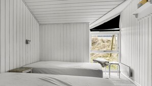 A room with two beds, a small table, and a window with a view of the outdoors. - Amazing home in Thisted with sauna (Thisted)