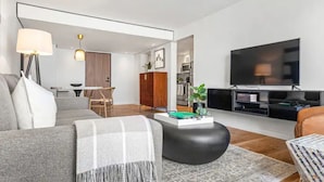 Un soggiorno moderno con un divano, un tavolino, una TV e, sullo sfondo, un'area pranzo.