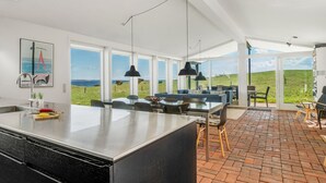 Ett modernt kök med en stor köksö, en matplats med stolar och utsikt över havet.