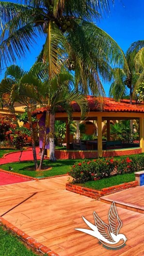 Guests may relax beneath the gazebo's red-tiled roof, surrounded by a well-maintained garden with lush greenery and vibrant flowers.
