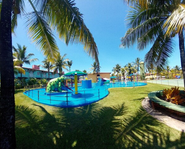 Relax by the pool surrounded by lush greenery and palm trees, with a frog-shaped slide for kids to enjoy.