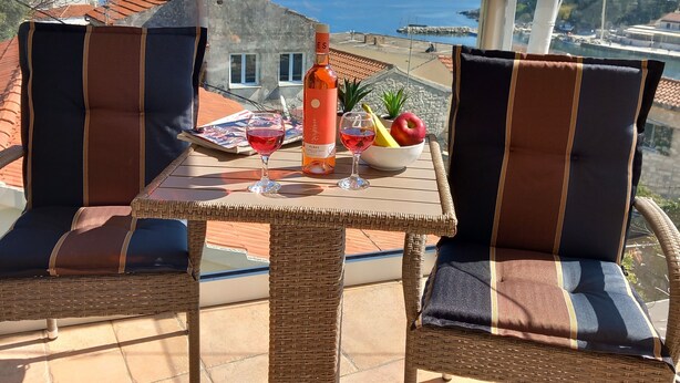 Een rieten tafeltje met twee stoelen, een fles wijn, een glas rode wijn, een schaal fruit en een menukaart.