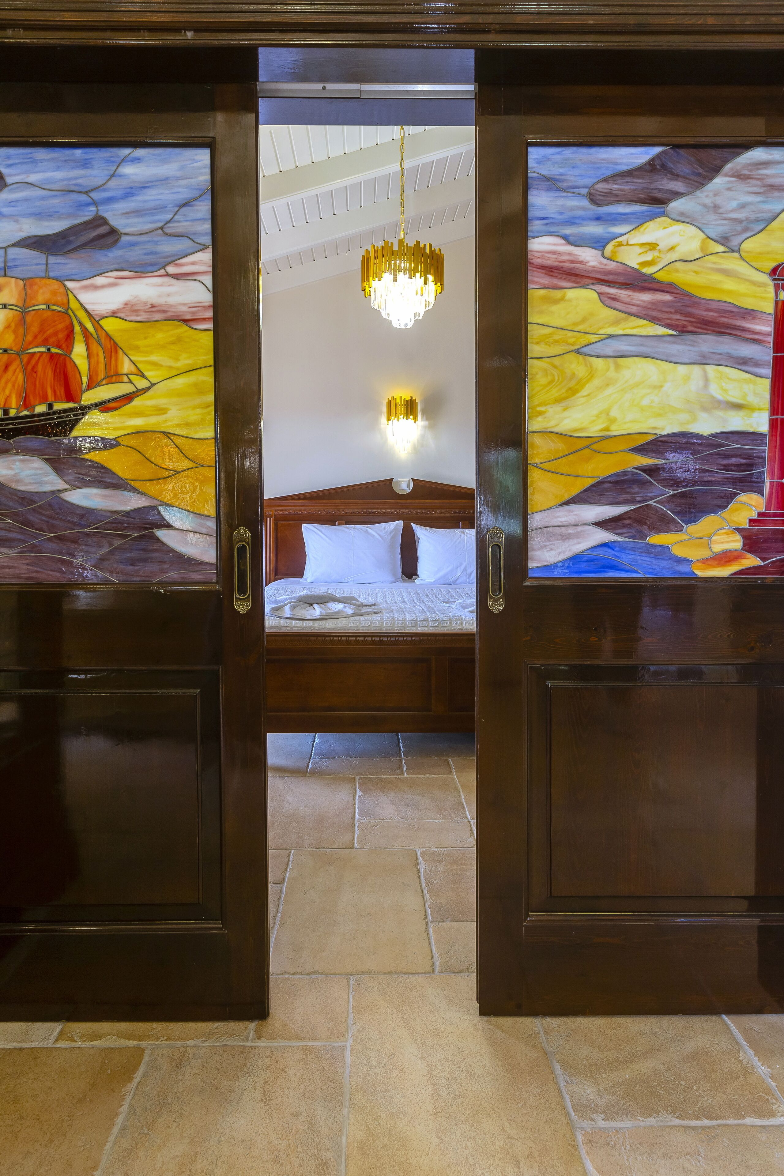 Quarto de hotel com uma cama grande, um lustre e uma janela de vitrais.