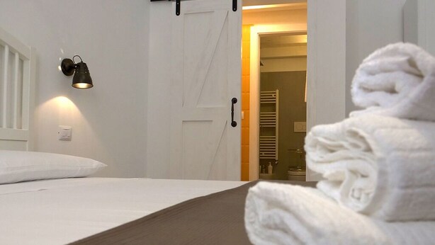 A neatly made bed with a white pillow, a folded white towel on the bed, and a wall-mounted light fixture. - Detached house in the center Cardille Apartment (Monopoli)