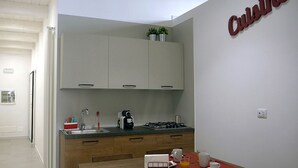 A modern kitchen with white cabinets, a sink, and a coffee maker. There's a table with a sign that reads "Service de Comptoir" and a red placemat. - Detached house in the center Cardille Apartment (Monopoli)