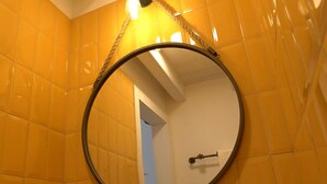 Ein Badezimmer mit gelben Fliesen, einem runden Spiegel und einer sichtbaren Tür zu einem anderen Raum.