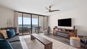 Una sala de estar moderna con sofá, mesa de centro y televisor. Hay un balcón con vistas.