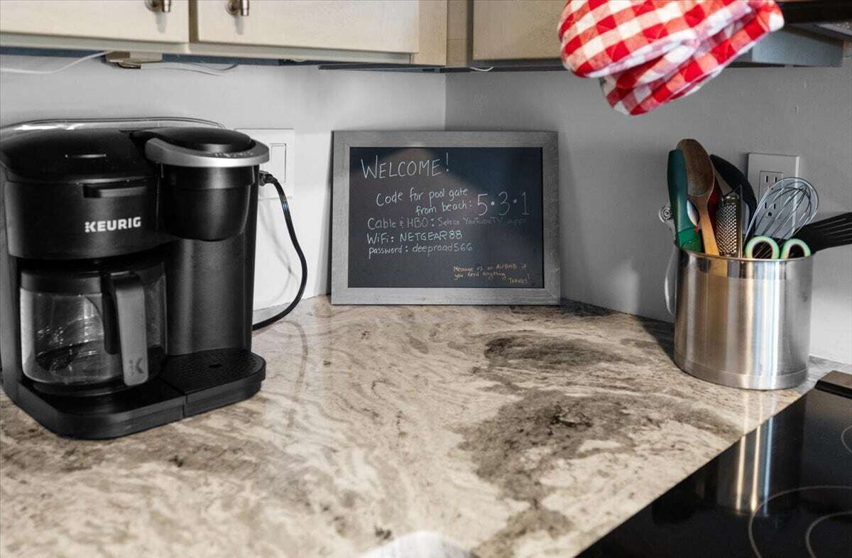 Una macchina da caffè, una lavagna con un messaggio di benvenuto e utensili da cucina su un piano di lavoro.