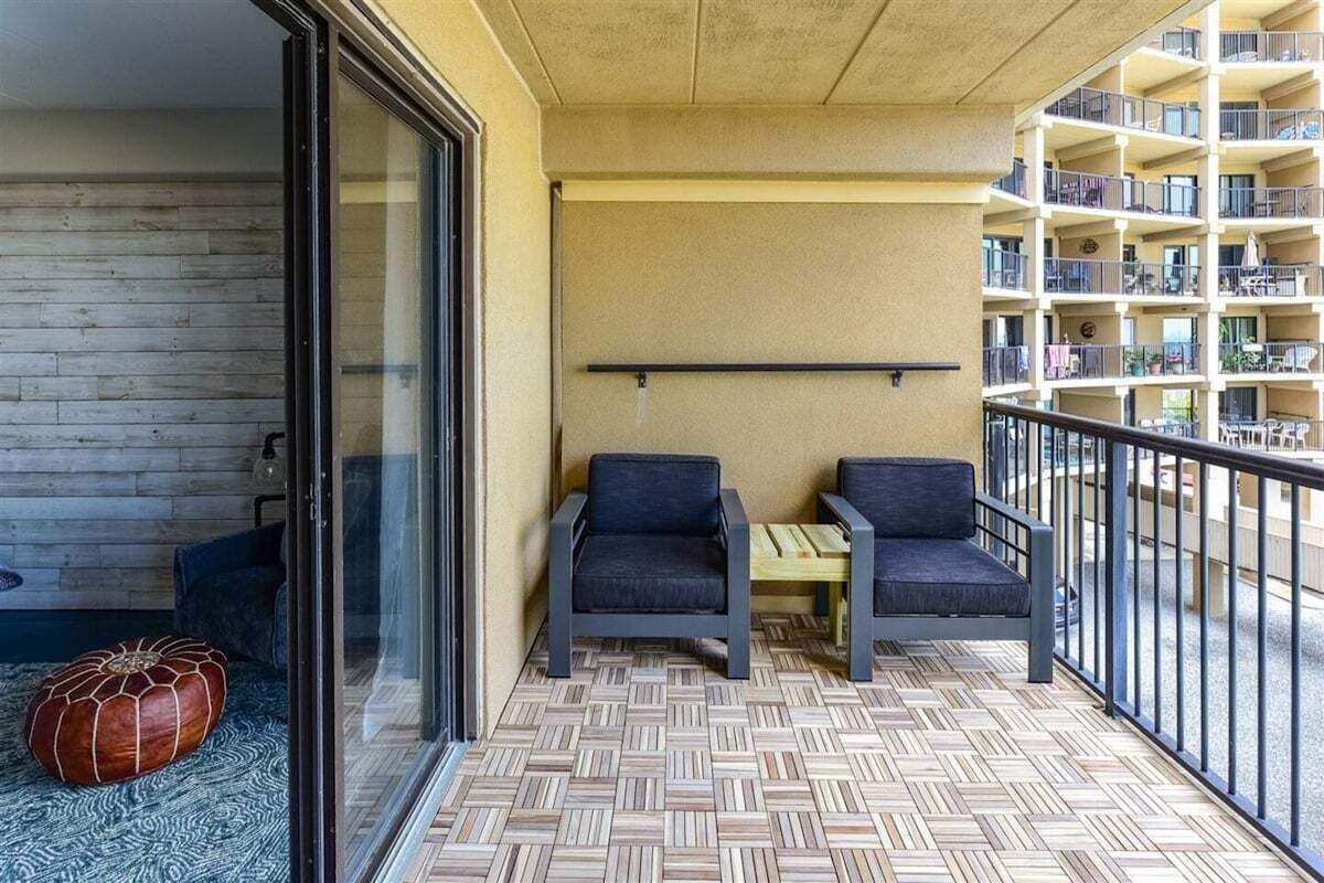 A balcony with two chairs and a small table, a wooden floor, and a view of an apartment building.
