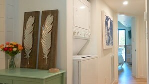 A hallway with a laundry room, decorative leaf wall art, and a green cabinet with a vase of flowers. - 2 Bdrm/2 Bath, Sleeps 6, Pool, Balcony, Wi-Fi, TVs (Ocean City)