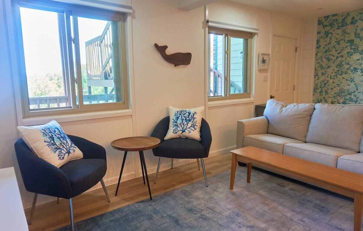 A living room with a sofa, two armchairs, a small round table, and a wooden bench.