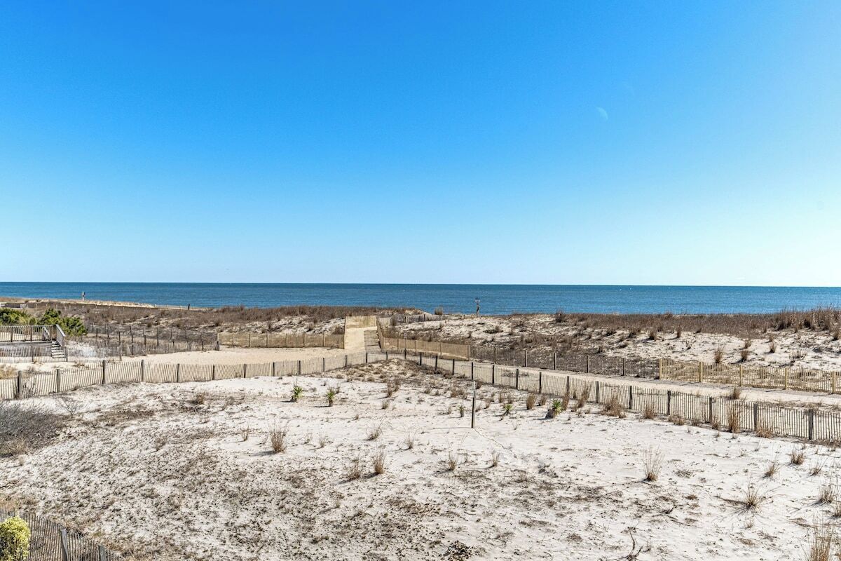 Ein Sandstrand mit einer Holzlattenzaun und freiem Blick auf das Meer.