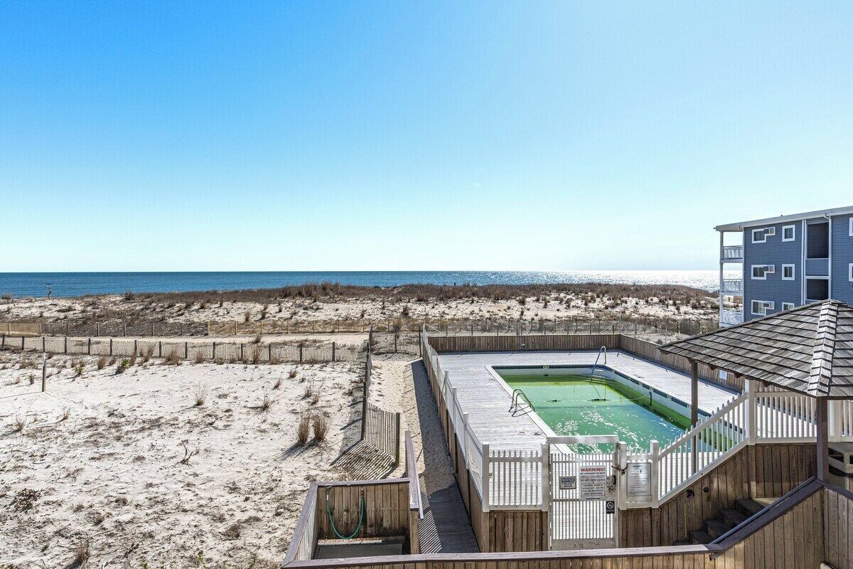 Un espace piscine situé au bord de la plage, avec une terrasse en bois, une piscine et une vue sur la plage et l’océan.