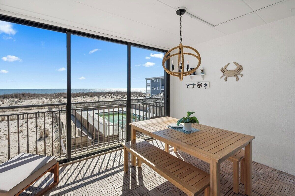 Uma varanda com mesa e banco de madeira, luminária pendente e vista para a praia e oceano.