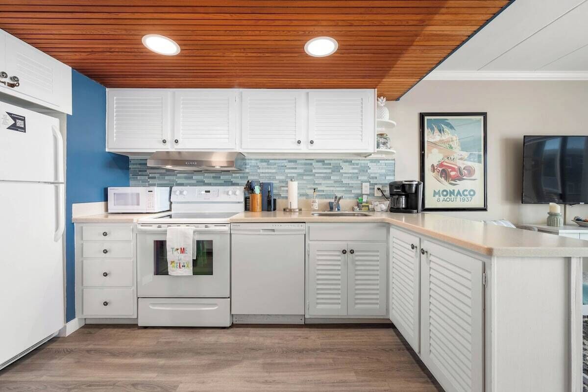 A modern kitchen with white cabinetry, a microwave, a stove, and a sink. There is a framed picture of a car on the wall.