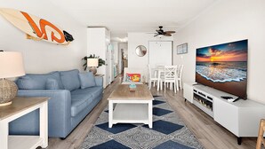 Ett modernt vardagsrum med en blå soffa, ett soffbord, en tv och en surfbräda som dekoration.
