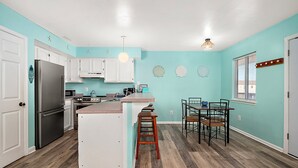 A kitchen with white cabinets, a stainless steel refrigerator, a wooden island with stools, and a dining area with a table and chairs.